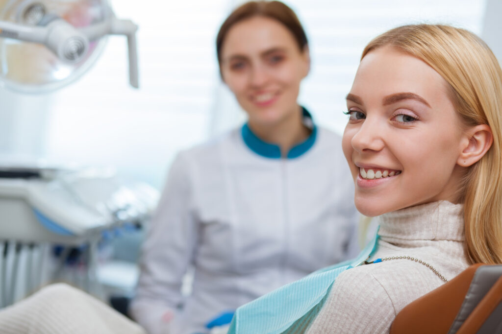 Gorgeous happy woman with perfect healthy teeth smiling to the camera, sitting at dental chair